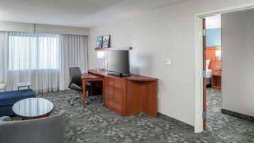 A hotel room with a desk, chair, television, and a small round table.