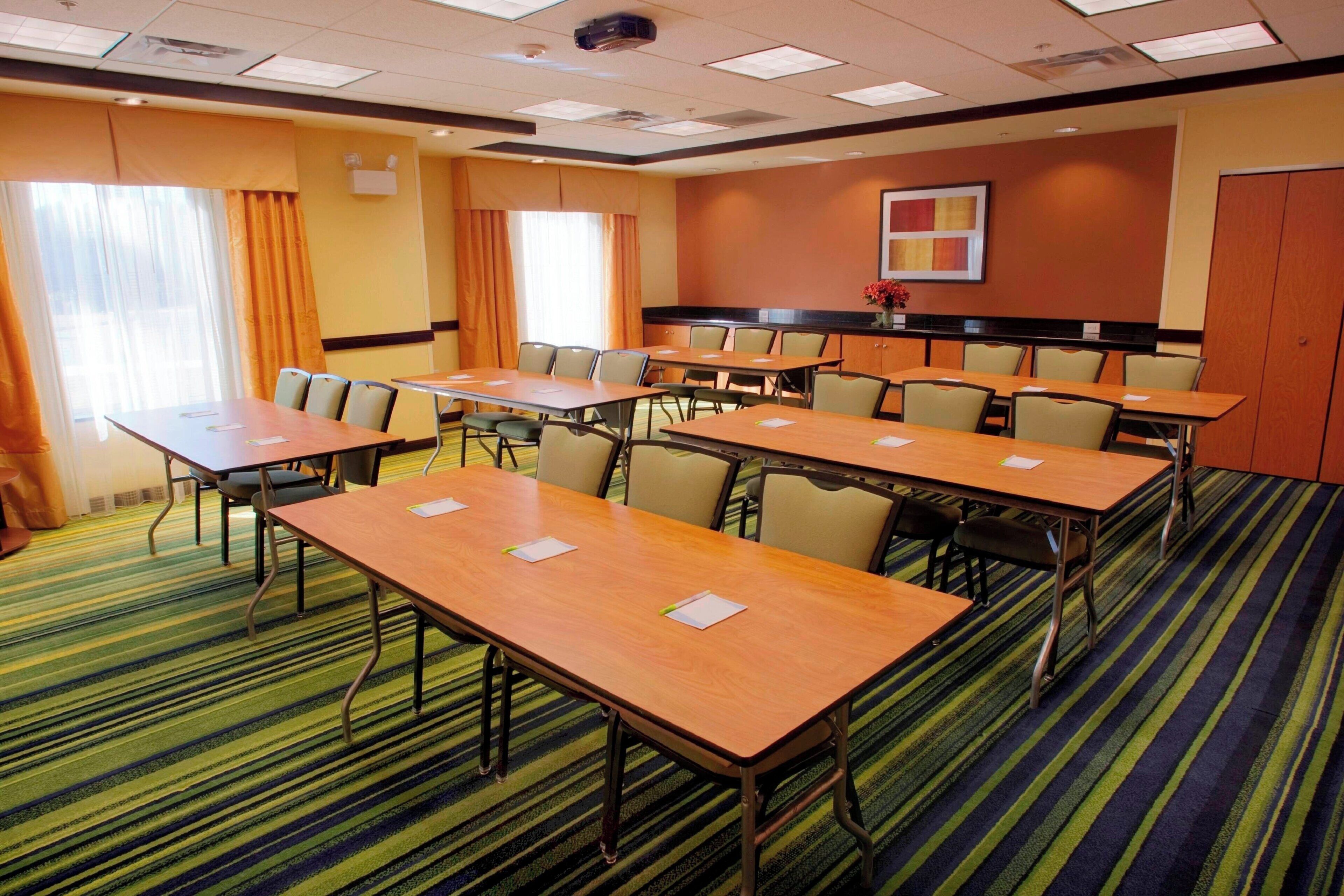 A conference room with multiple tables and chairs, carpeted floor, and large windows with curtains.