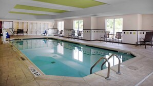 Una piscina interior con agua cristalina, rodeada de sillas y mesas, y un suelo de baldosas.