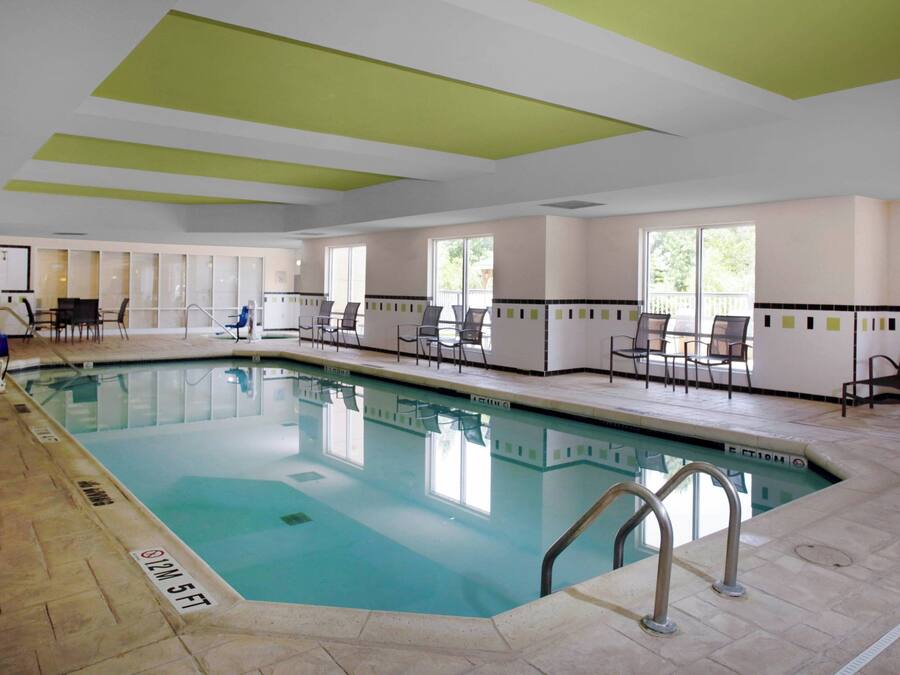 An indoor swimming pool with clear water, surrounded by chairs and tables, and a tiled floor.