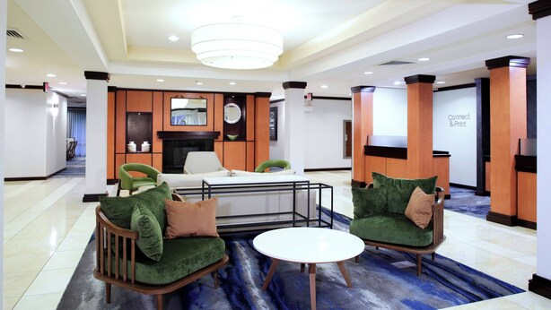 Un vestíbulo con diseño moderno, que incluye una zona de estar con sillones tapizados en verde, una mesa de centro blanca y una alfombra decorativa.