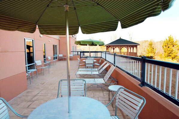 Un patio al aire libre con sillas y mesas de metal, un pabellón y una zona cubierta con sombrillas.