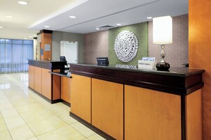 Zona de recepción de un hotel con un mostrador de madera, un adorno en la pared, un cartel de Marriott Bonvoy y una lámpara.