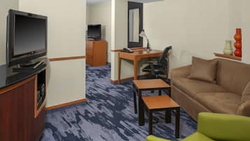 Habitación de hotel con televisión, escritorio, silla, sofá y una pequeña mesa.