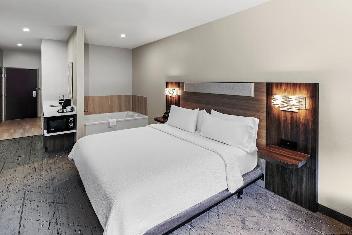 Ein modernes Hotelzimmer mit einem großen Bett, einem fest installierten Schreibtisch, einer Badewanne und einer Wandleuchte.