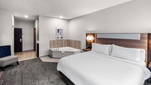 A modern hotel room with a large bed, a separate bathroom with a bathtub, a small seating area, and a wooden headboard. - Holiday Inn Express and Suites Henderson by IHG (Henderson)