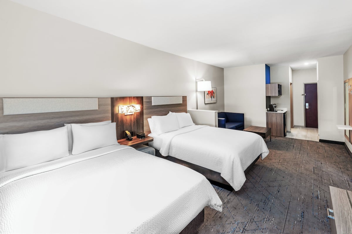 Ein Hotelzimmer mit zwei Betten, einem Schreibtisch, einem Stuhl, einer Lampe und einem Fernseher.