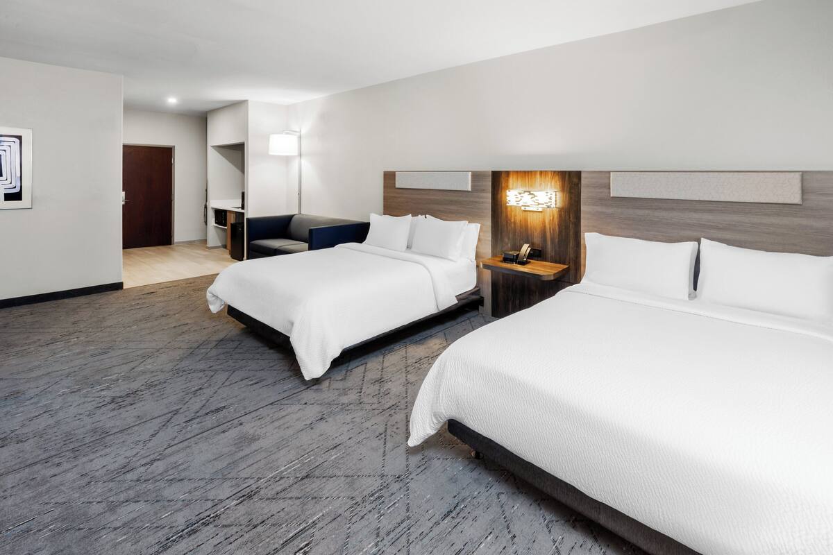 Ein Hotelzimmer mit zwei Betten, einem Schreibtisch, einem Stuhl, einer Lampe und einer Tür.