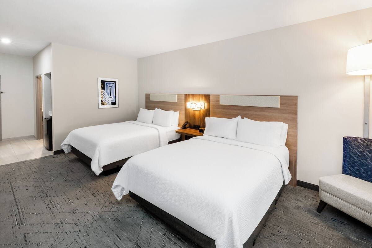 Ein Hotelzimmer mit zwei Betten, einem Nachttisch, einer Lampe und einem Sessel.