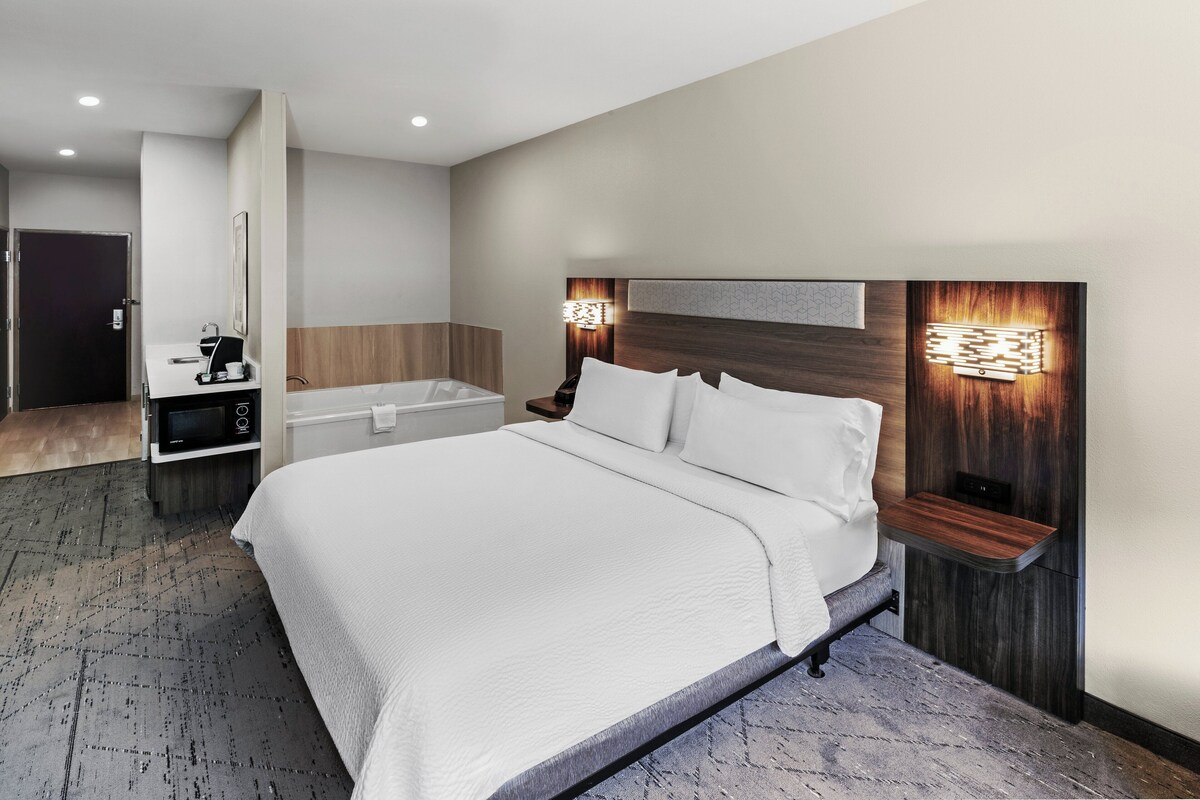 Una habitación de hotel moderna con una cama grande, un escritorio integrado, una bañera y una lámpara fijada a la pared.