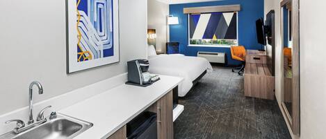 A modern hotel room with a kitchenette, a bed, a desk, and a large window with a view.