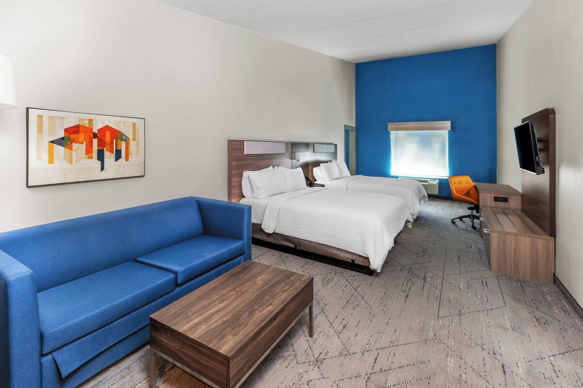 Ein Hotelzimmer mit blauem Sofa, zwei Betten, einem Holztisch, einem Fernseher und einem Gemälde an der Wand.