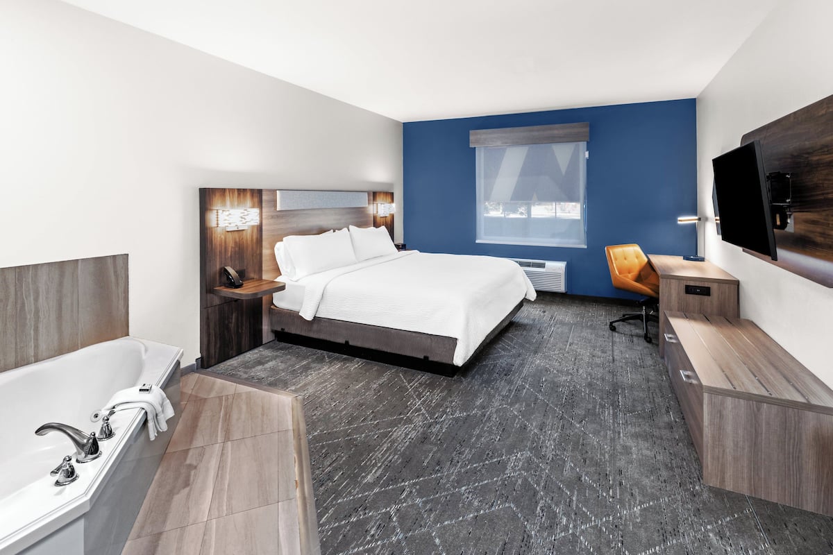 Ein modernes Hotelzimmer mit einem großen Bett, einem separaten Badezimmer mit einer Badewanne, einem Schreibtisch und einem Fernseher.