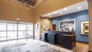 A lobby with a large patterned rug, a reception desk, framed pictures on the wall, and an exit sign. - Hampton Inn & Suites Huntsville Hampton Cove (Brownsboro)