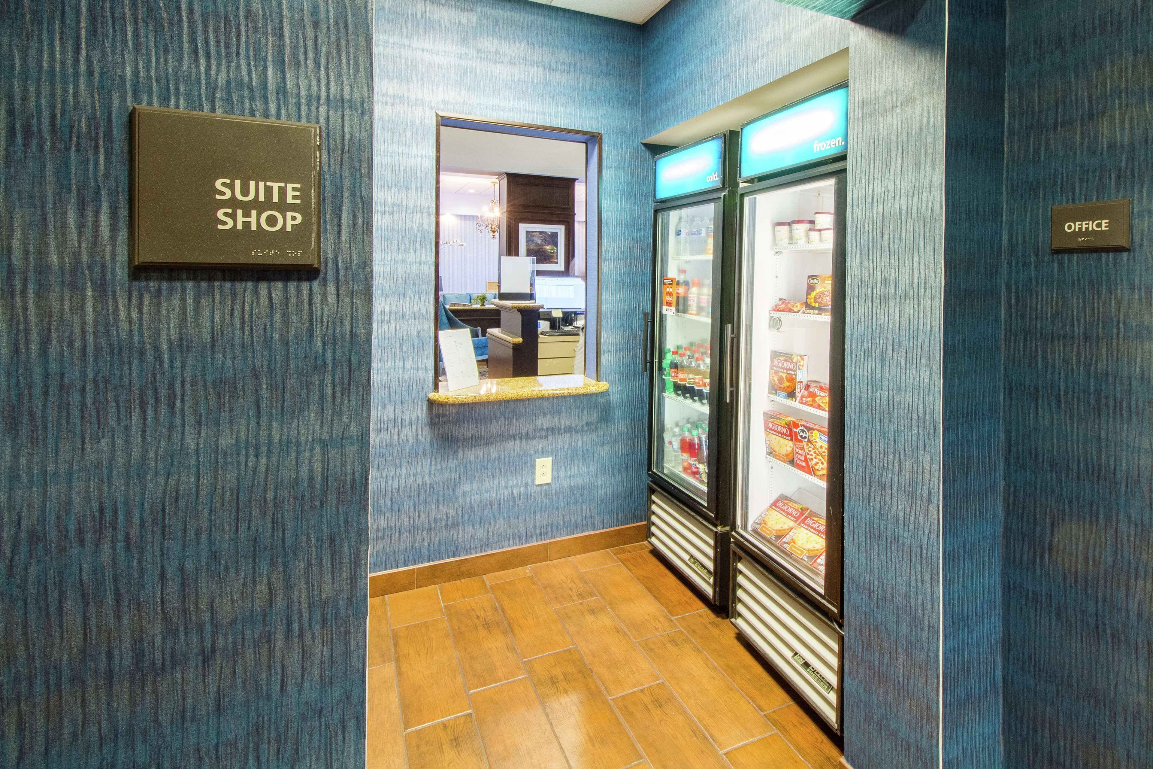 Un corridoio di hotel con un cartello 'SUITE SHOP', uno specchio e una vetrina refrigerata.