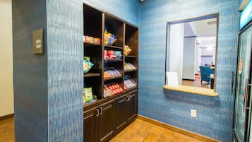 A hotel corridor with a blue textured wall, a wooden cabinet with snacks, and a small window with a mirror.