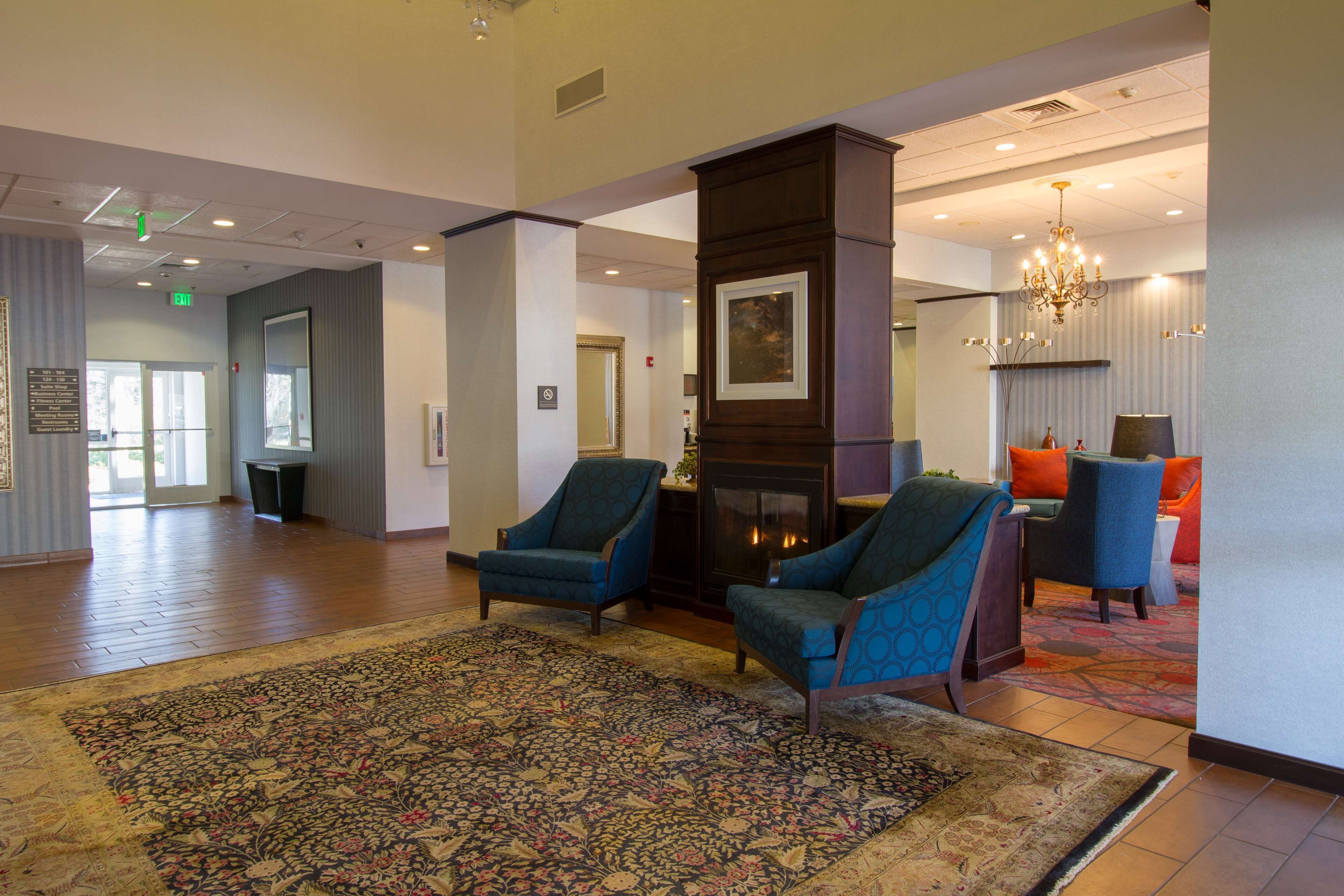 A lobby with a large rug, two blue armchairs, a fireplace, and a chandelier.