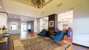 A spacious lobby with a large carpet, two blue armchairs, a fireplace, and a chandelier. - Hampton Inn & Suites Huntsville Hampton Cove (Brownsboro)