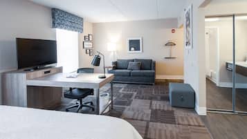 Una habitación de hotel moderna con una cama, un escritorio con computadora, un televisor, un sofá y una mesita.
