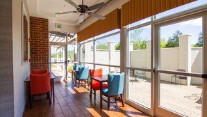 A covered outdoor seating area with brick walls, large windows, and a ceiling fan. - Hampton Inn & Suites Huntsville Hampton Cove (Brownsboro)
