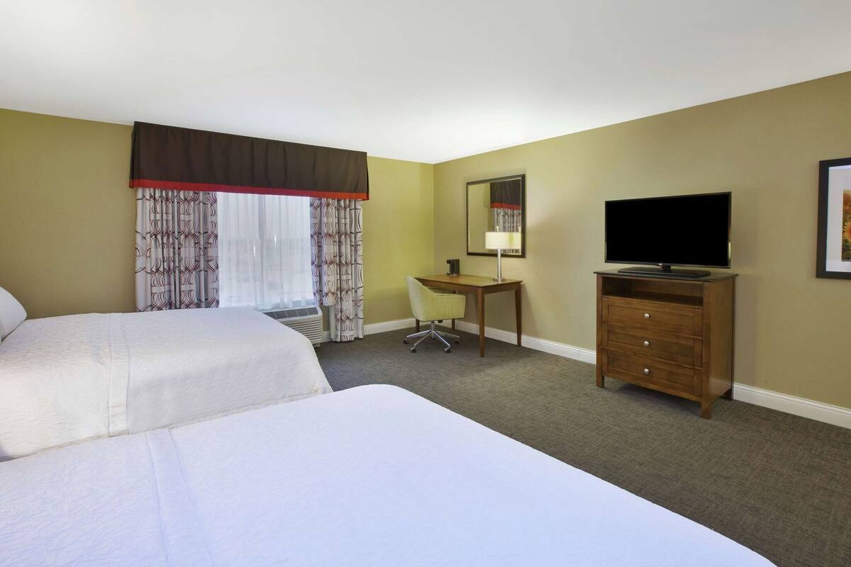 A hotel room with two beds, a desk, a television, and a mirror.