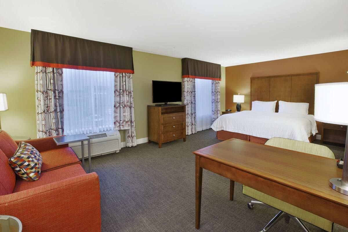A hotel room with a bed, a desk, a TV, a dresser, and a sofa.