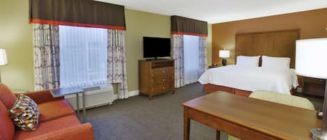 A hotel room with a bed, a desk, a TV, a dresser, and a sofa.