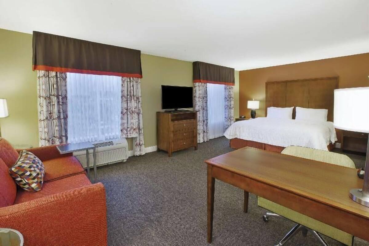 A hotel room with a bed, a desk, a television, and a sofa.