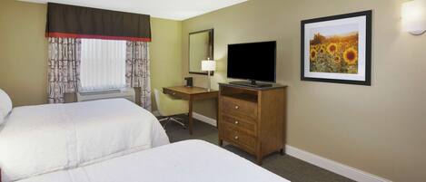 A hotel room with two beds, a desk, a television, a lamp, and a framed picture on the wall.