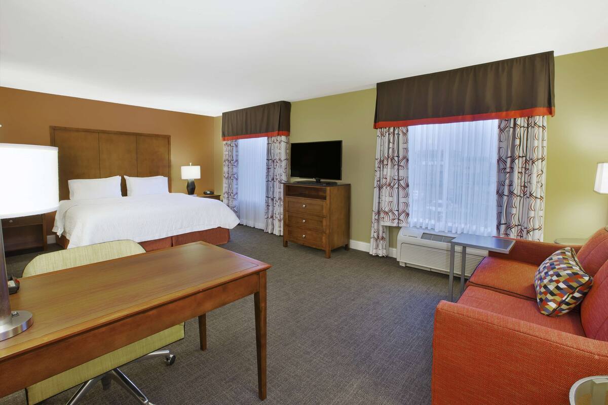 A hotel room with a bed, a desk, a TV, a dresser, and a sofa.