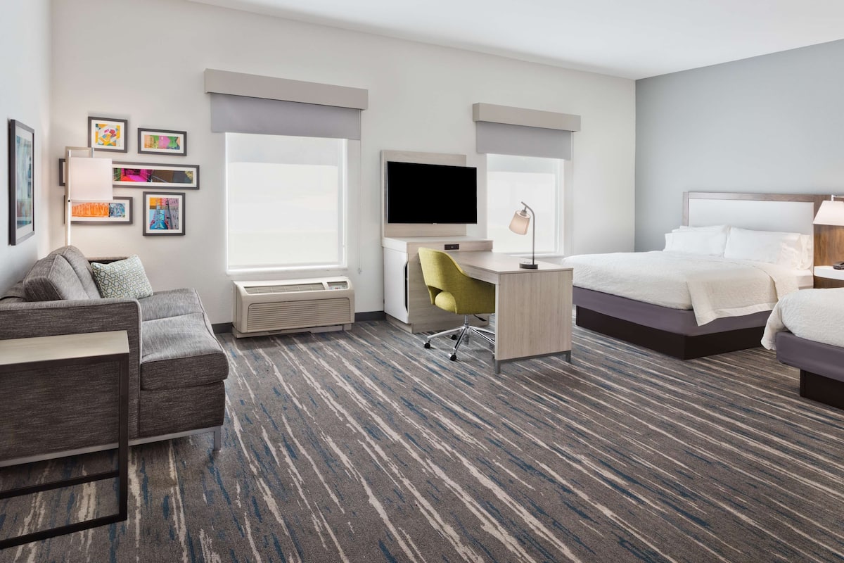 A hotel room with a bed, a desk with a chair, a TV, and a couch.