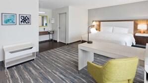 Een hotelkamer met een bed, nachtkastje, stoel, bureau en een badkamer met wastafel en spiegel.