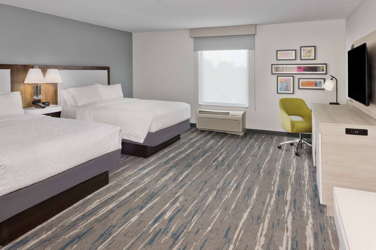 A hotel room with two beds, a desk, a chair, a TV, and a window with a view.