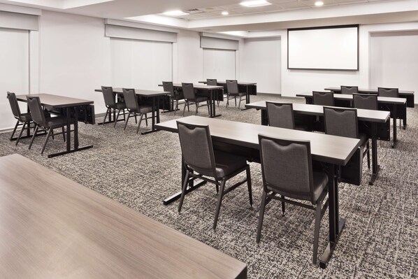 A conference room with multiple tables and chairs, carpeted flooring, white walls, and a projector screen. - Hampton Inn & Suites Phenix City- Columbus Area (Phenix City)