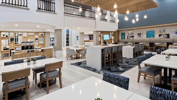 Een moderne hotel lobby met een bar in het midden, zitgedeeltes en een keuken op de achtergrond.