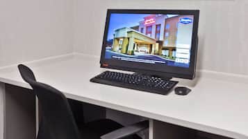 A computer monitor displaying a hotel website, a keyboard, a mouse, and a black office chair.