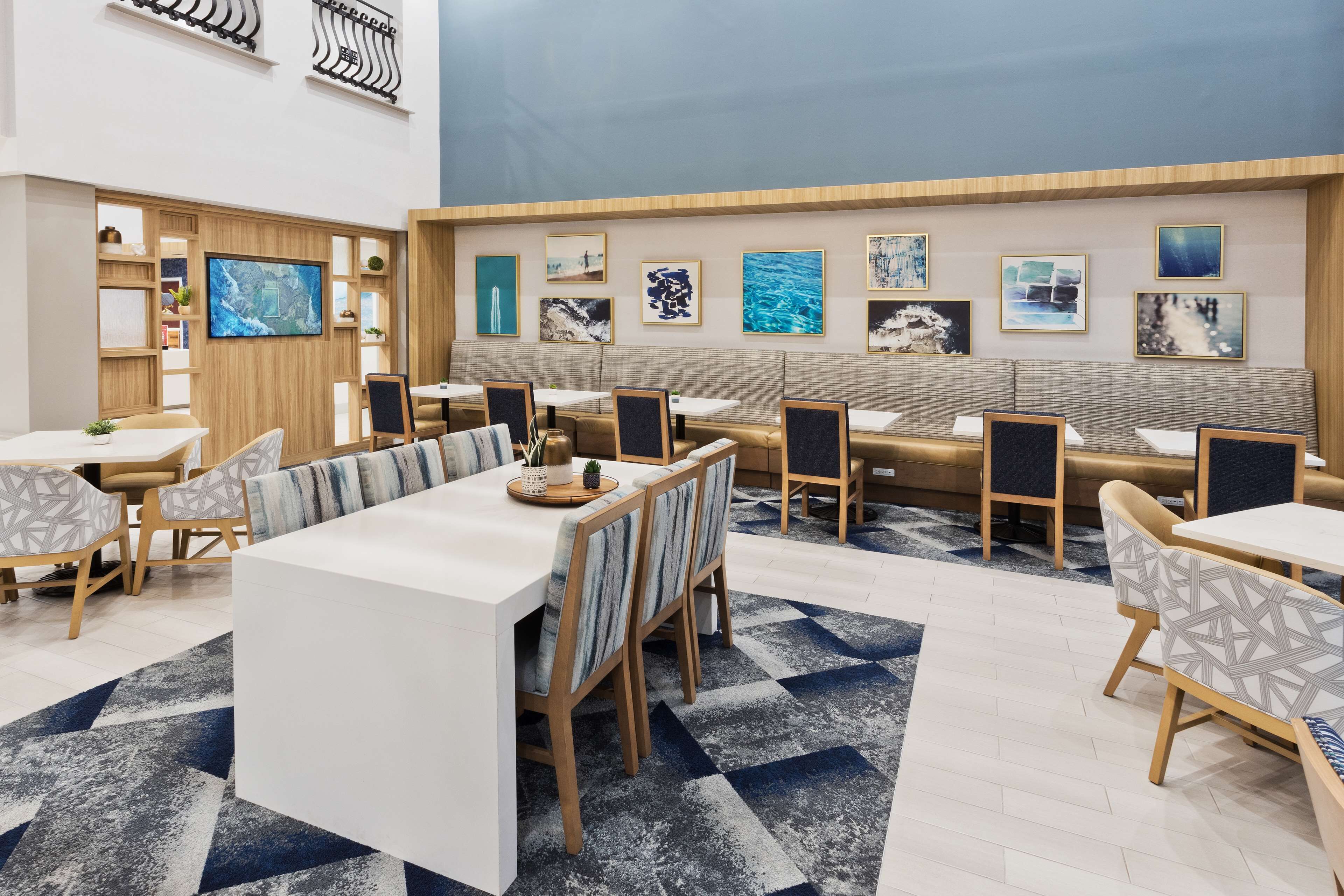 A modern hotel lobby with a central seating area, a TV mounted on a wooden panel, and artwork on the walls.