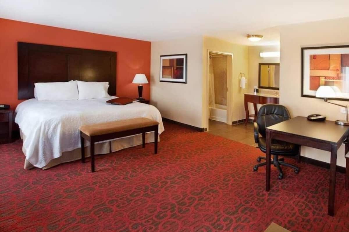 A hotel room with a bed, desk, chair, and a bathroom door.