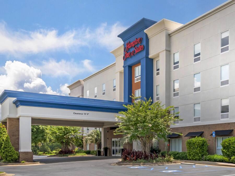 A Hampton Inn & Suites hotel with a clear sky, parking area, and greenery around.