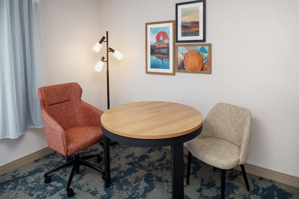 Um quarto com uma mesa redonda de madeira, duas cadeiras, um abajur e três obras de arte emolduradas na parede.