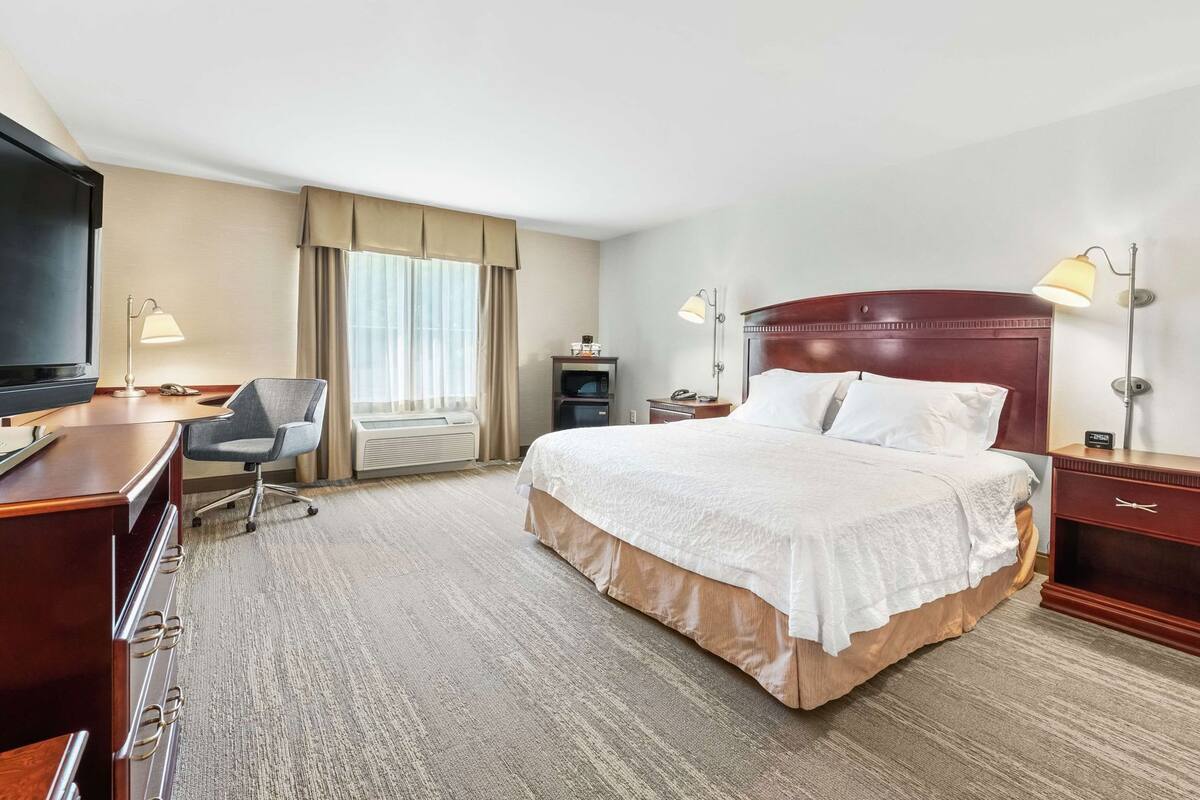 Quarto de hotel com cama, escrivaninha, cadeira, televisão e abajures.