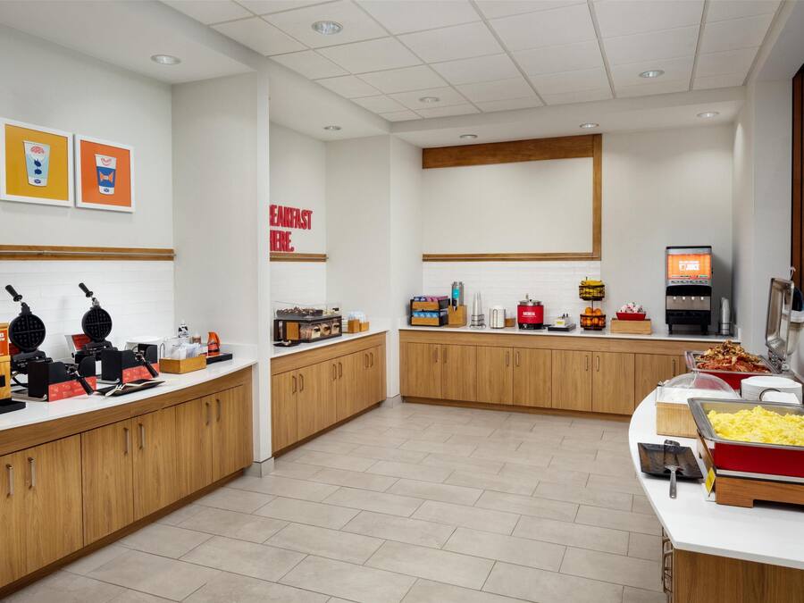 A breakfast buffet area with waffle makers, a coffee station, and various food items.