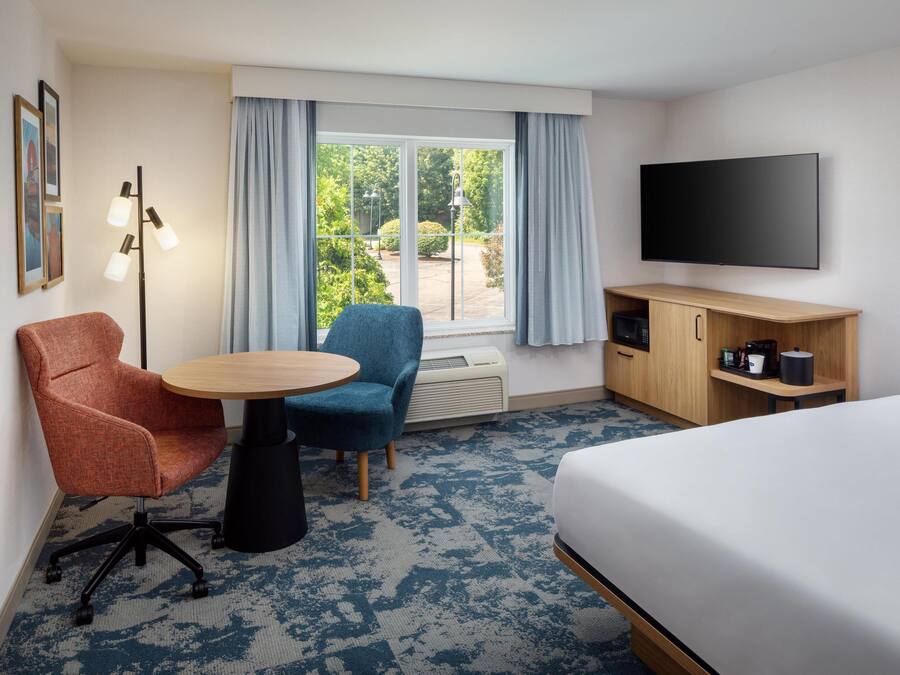 Une chambre d’hôtel avec un lit, un bureau, une chaise, une télévision et une fenêtre avec des rideaux.