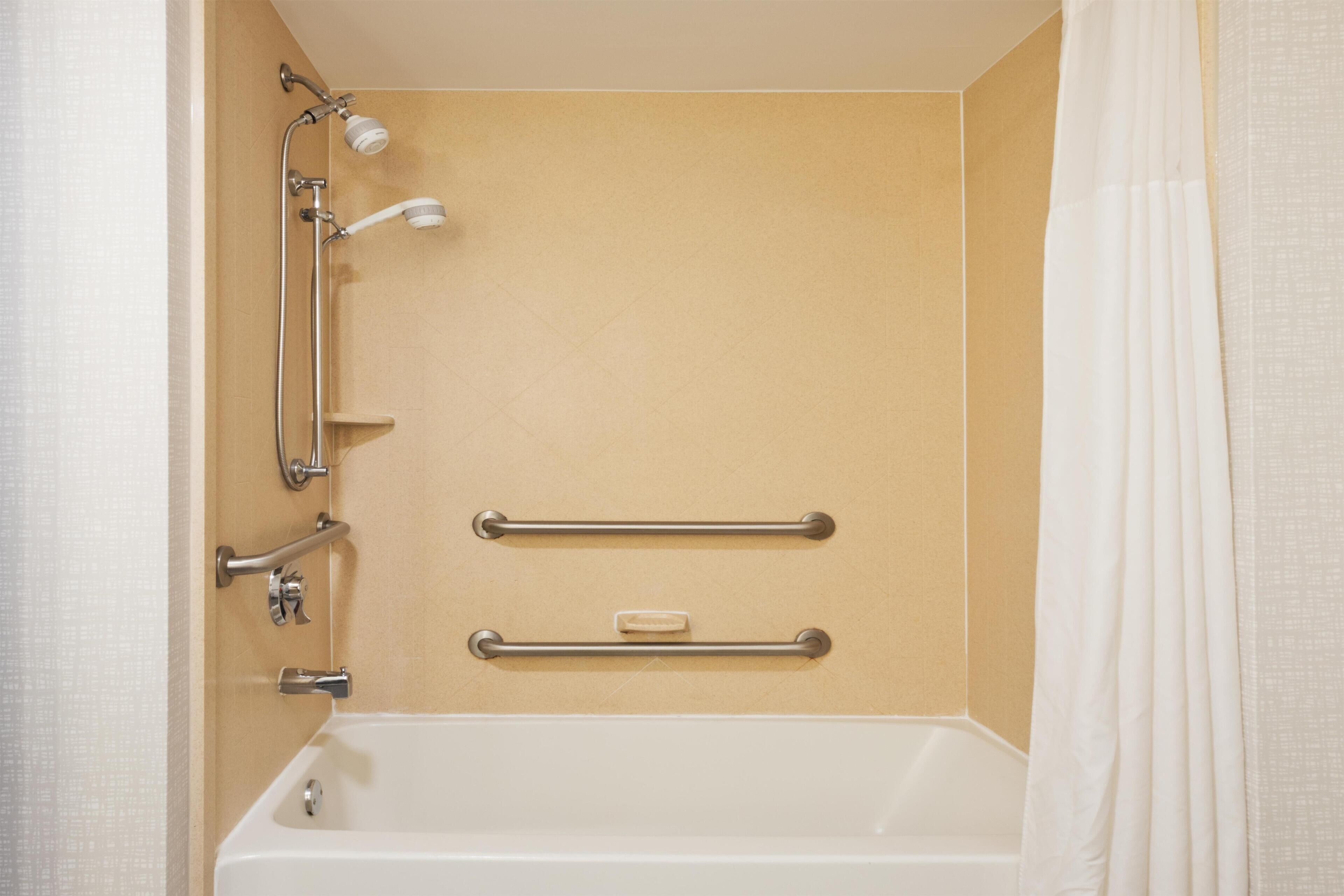 A bathroom with a bathtub, shower, grab bars, and a soap dish.