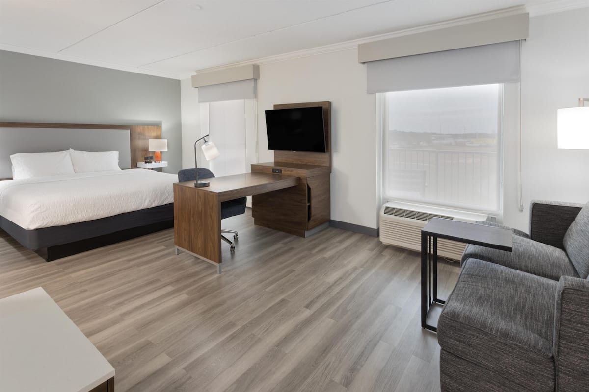A hotel room with a bed, desk, chair, TV, and a large window.