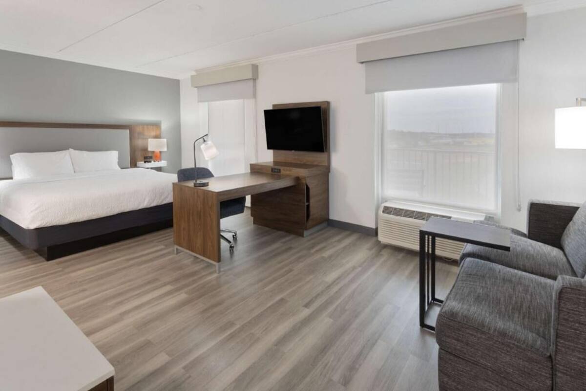 A hotel room with a bed, desk, TV, and a view of the city.