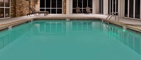 Una piscina con sillas de descanso y un muro de piedra.