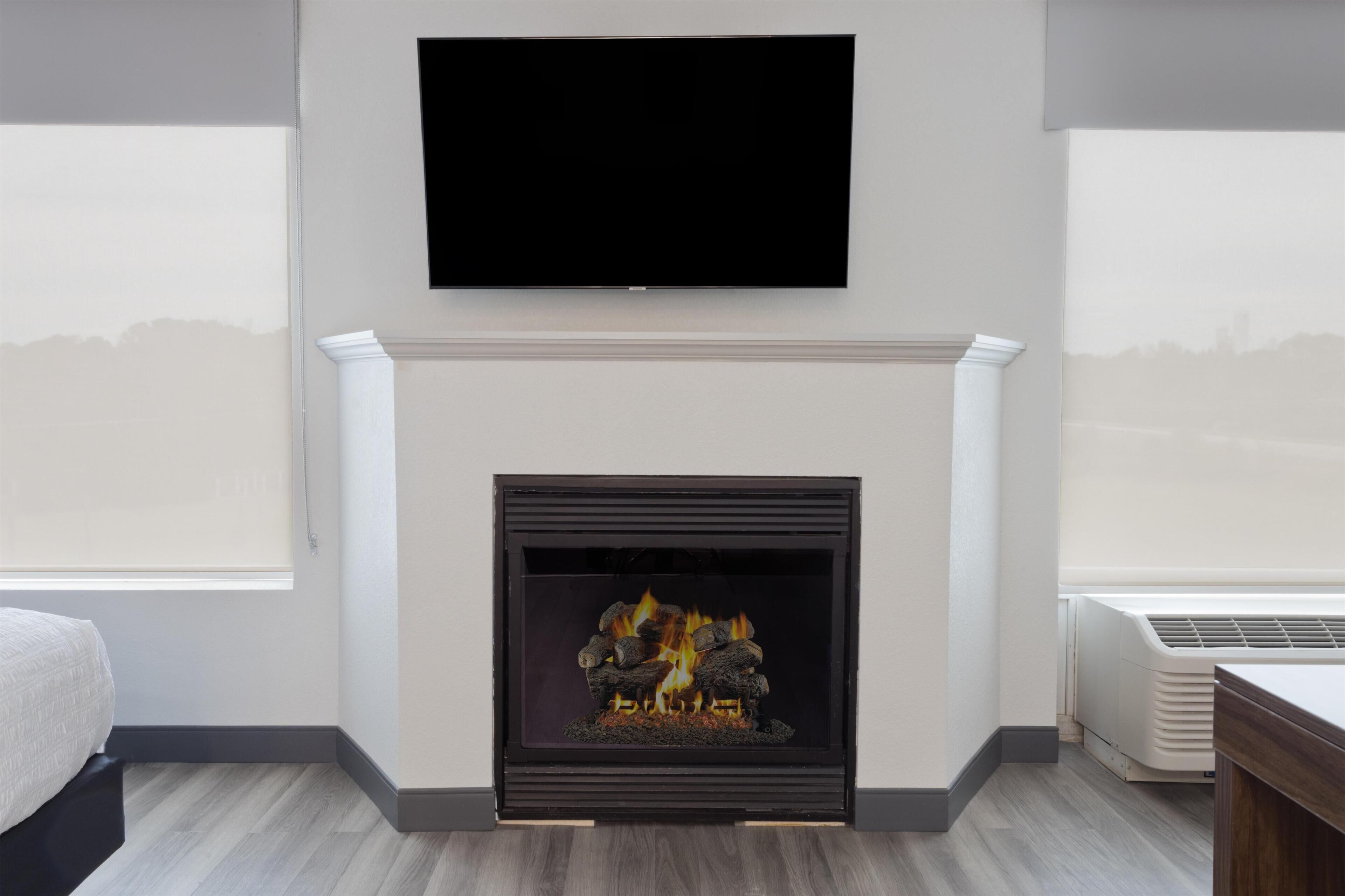 Una habitación moderna con chimenea, televisor montado y un amplio ventanal.