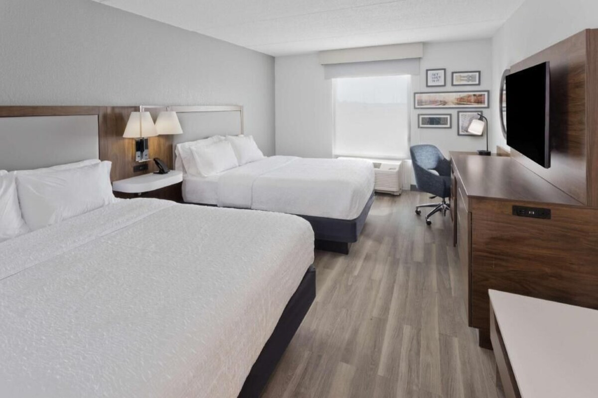 Une chambre d’hôtel avec deux lits, un bureau, une chaise, une télévision et une fenêtre.