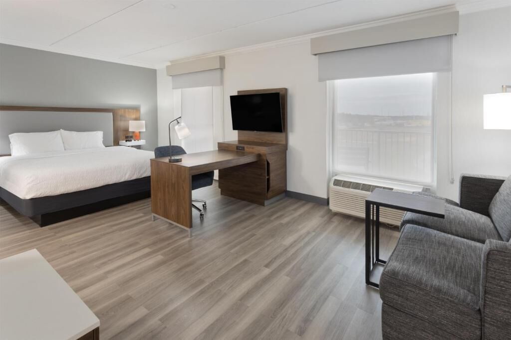 A hotel room with a bed, desk, chair, TV, and a view of the city.